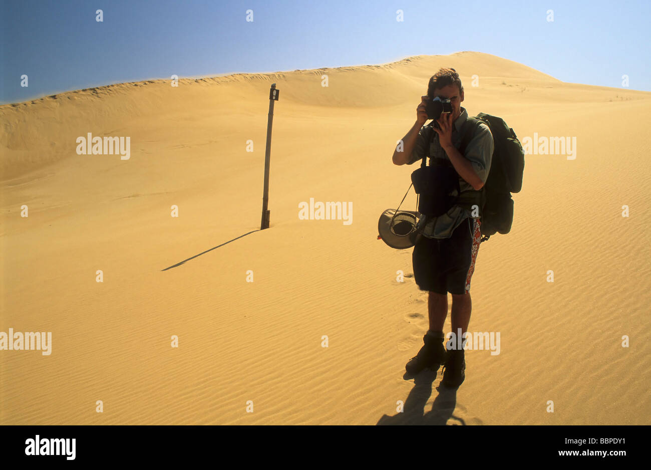 Randonneur avec caméra sur les dunes de sable avec route marqueur dans la distance moyenne dans le champ de dunes d'Alexandrie, Eastern Cape Afrique du Sud Banque D'Images