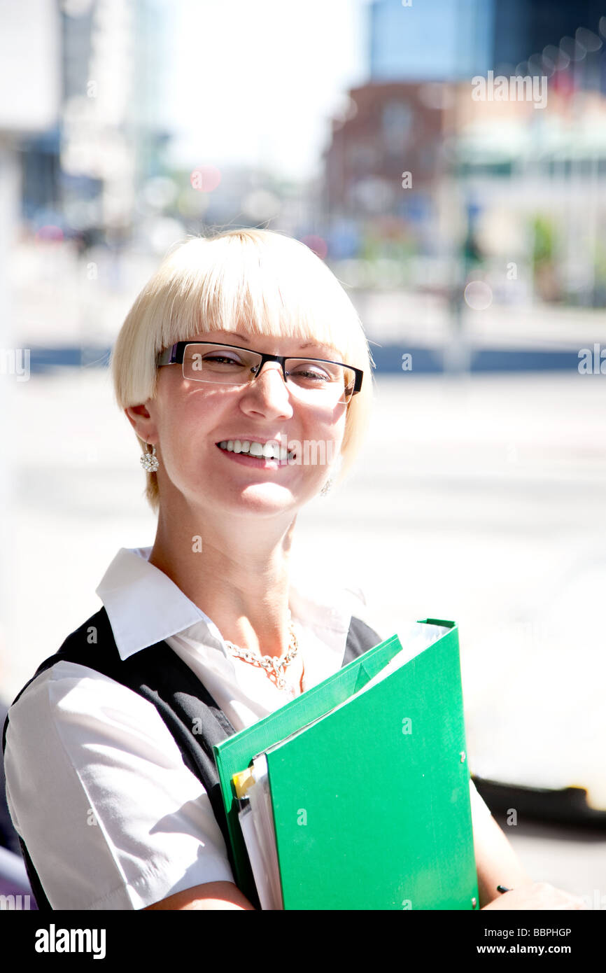 A smiling blonde jeune fille dans un costume blanc noir tenant un dossier vert Banque D'Images