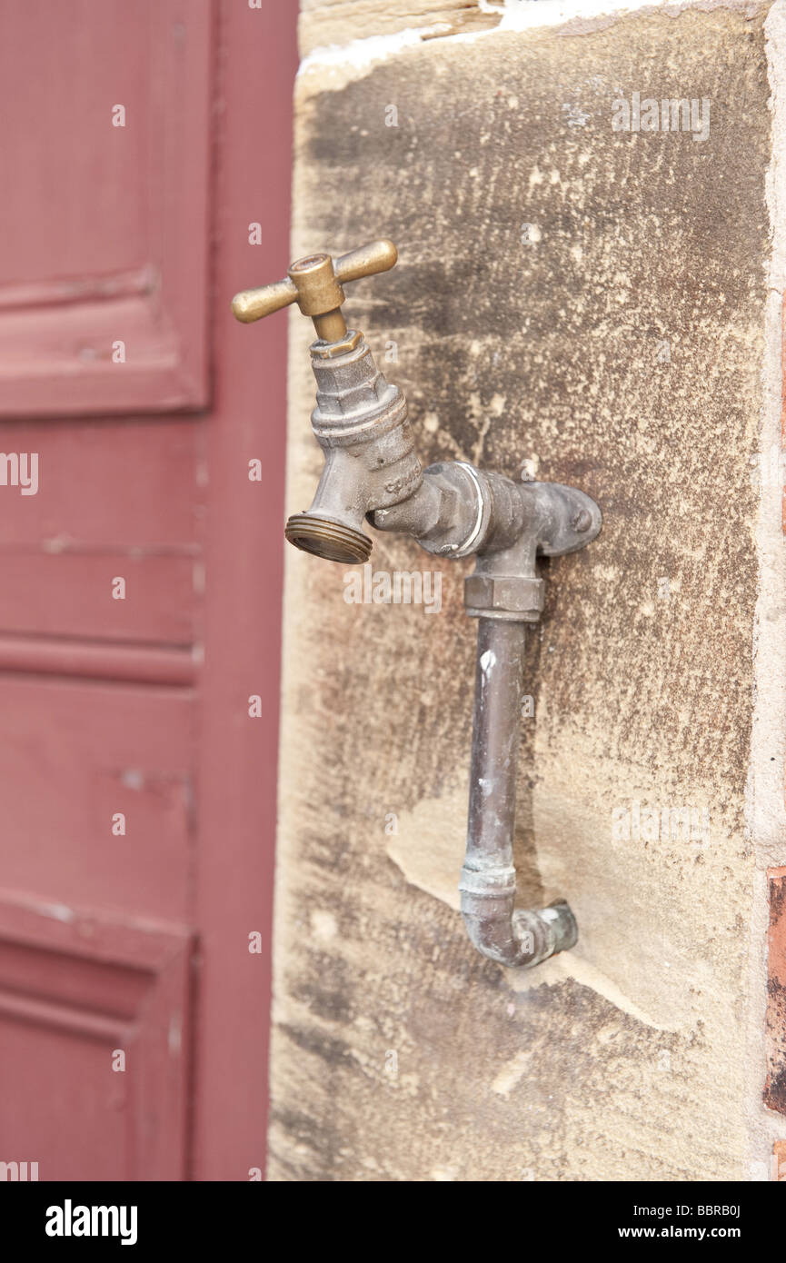 Externe en laiton/hors de l'eau du robinet de l'utilitaire installé sur la paroi de grès texturé avec porte en bois pâle Banque D'Images