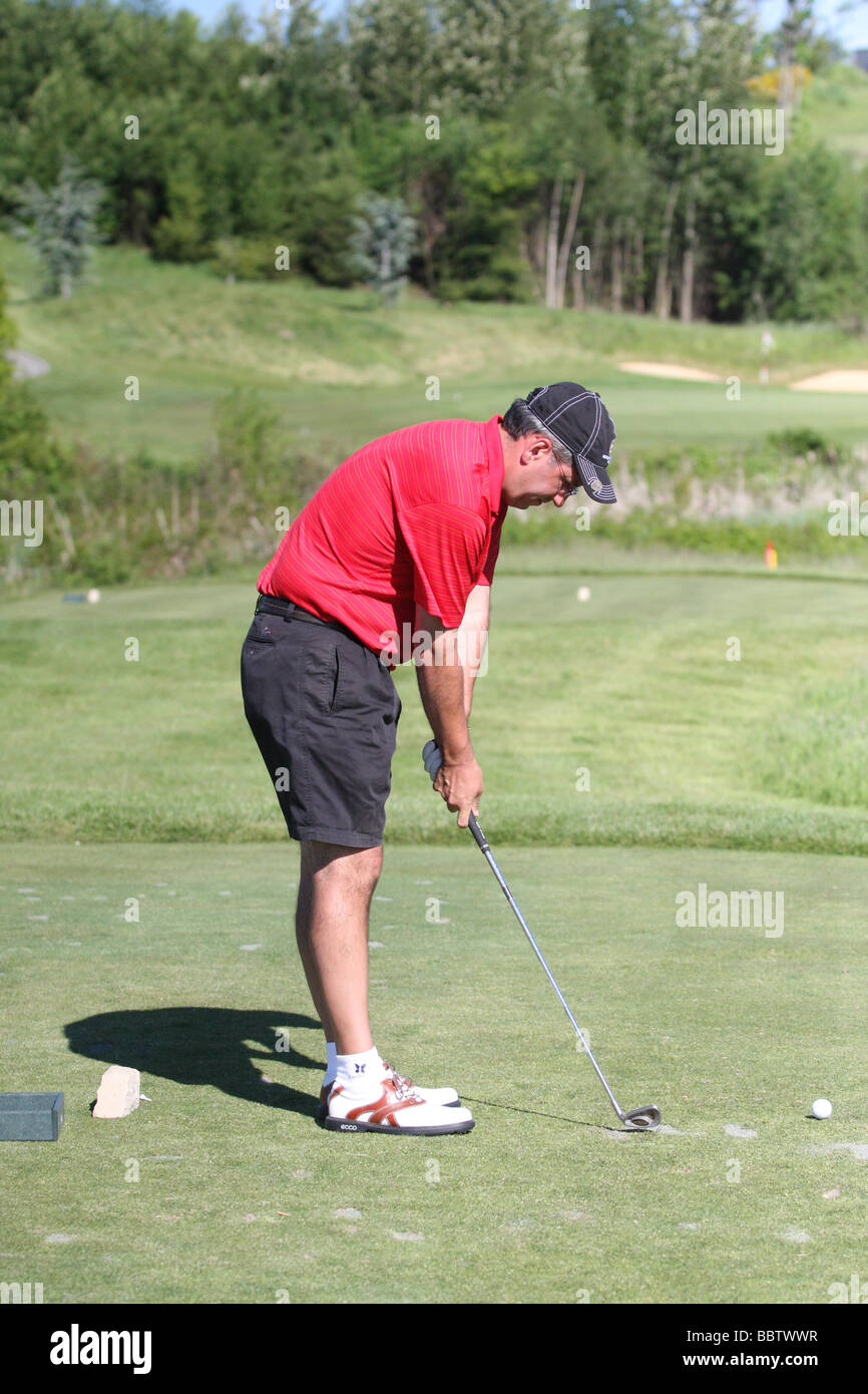 Un golfeur mâle passe par son swing de routine de préparation avant de frapper son coup de départ avec un fer à repasser à partir de la boîte de pièce en t d'un pair 3. Banque D'Images