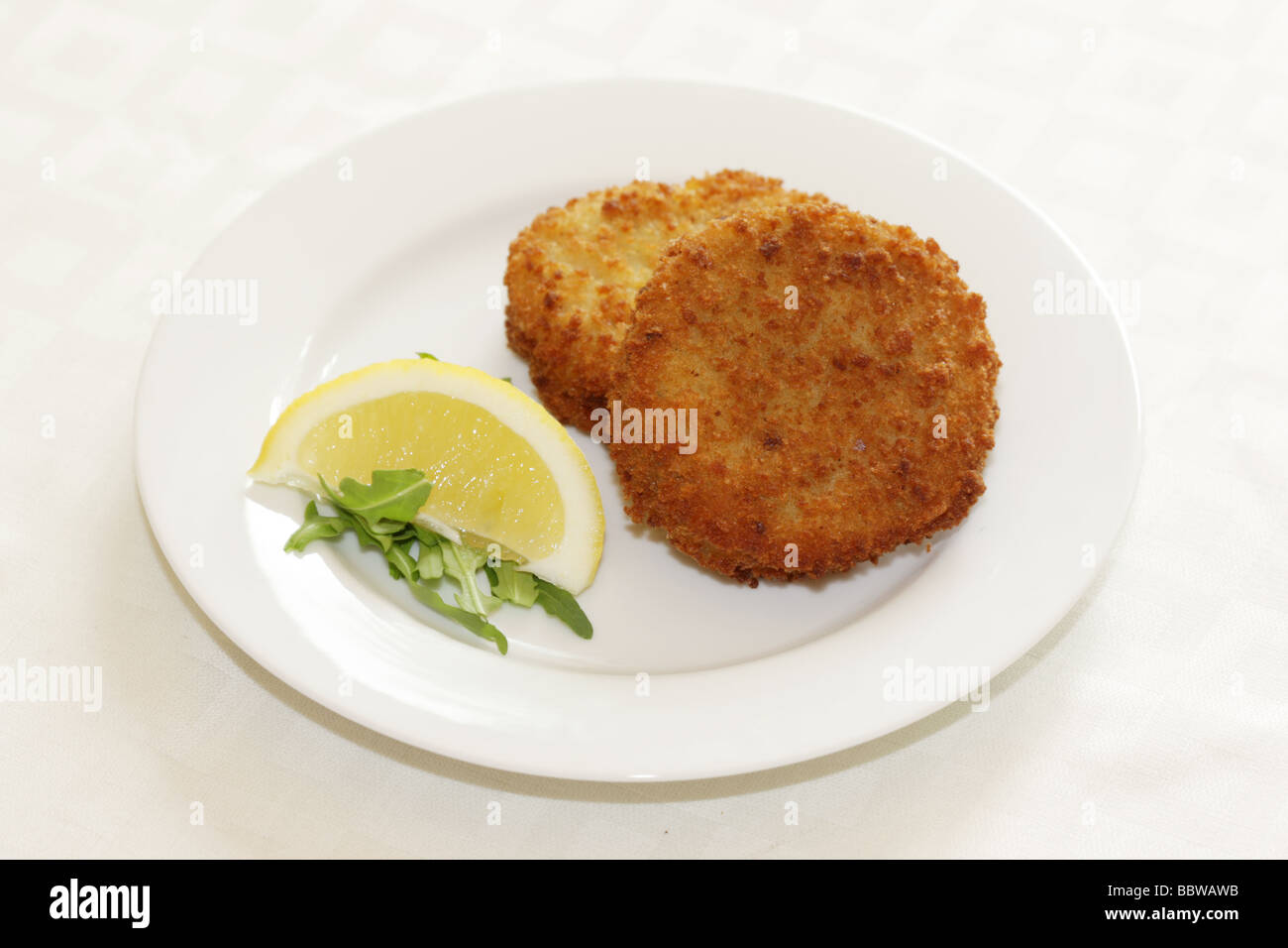 La morue panés délicieux fraîchement préparés Fishcakes avec citron et garnir de feuilles de salade isolé sur un fond blanc avec aucun peuple et un chemin de détourage Banque D'Images