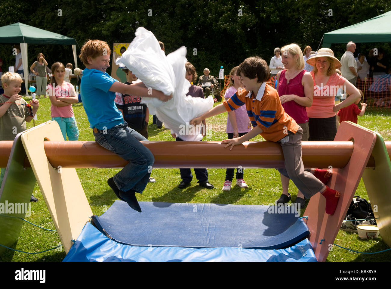 Les enfants ayant un oreiller lutte sur le terrain glissant de la pole position à une école summer fete, Medstead, Alton, Hampshire, Royaume-Uni. Banque D'Images