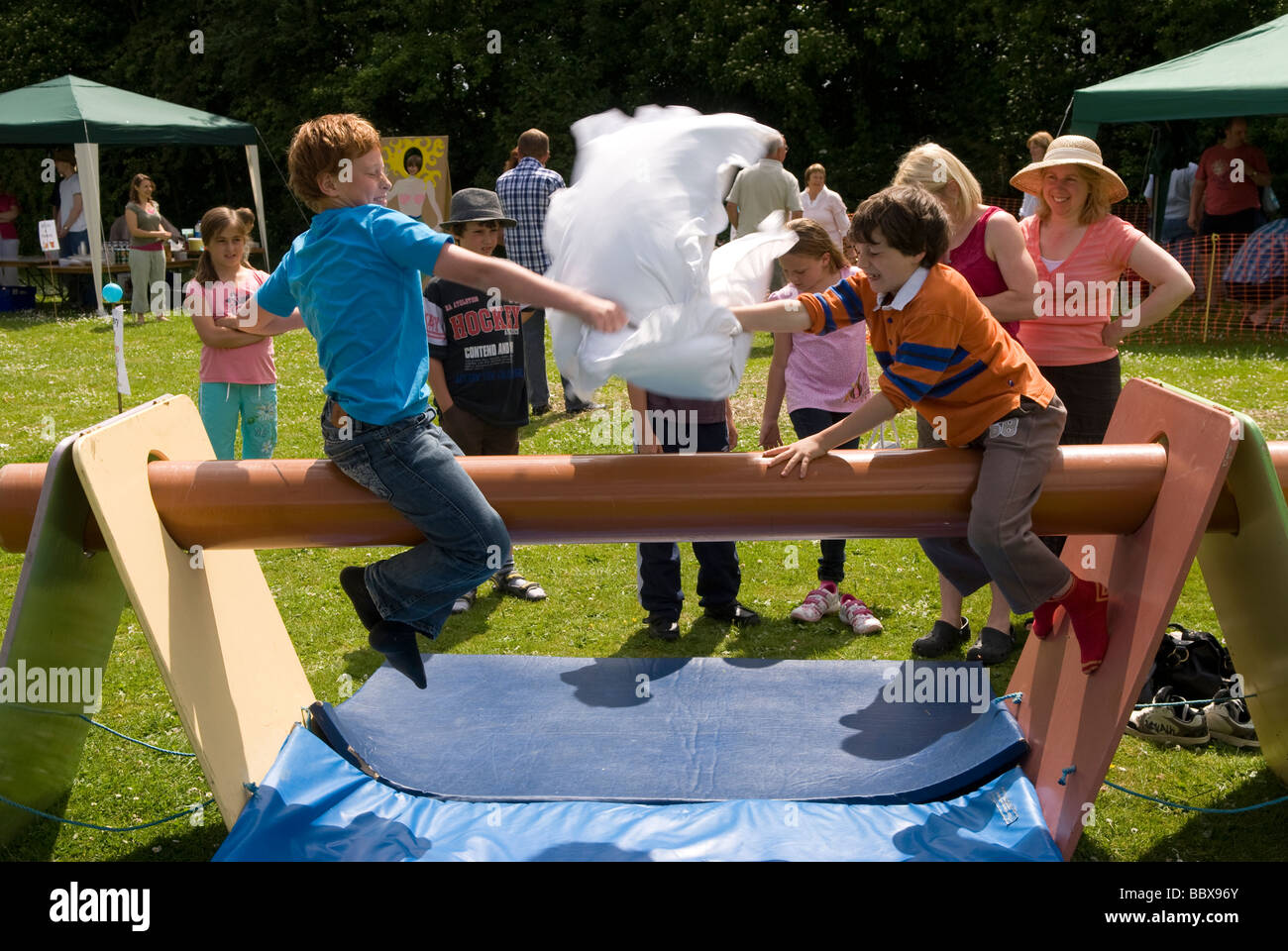 Les enfants ayant un oreiller lutte sur le terrain glissant de la pole position à une école summer fete, Medstead, Alton, Hampshire, Royaume-Uni. Banque D'Images