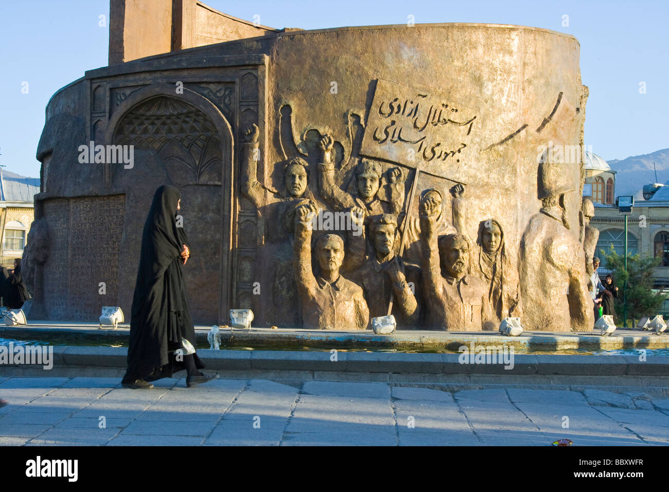 Femme portant un tchador comme elle passe devant un monument à la révolution dans l'Imam Khomeini Square à Hamadan Iran Banque D'Images