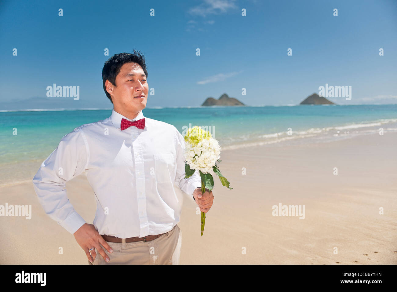 Asian groom attend que son épouse avec un bouquet de fleurs lors d'une promenade sur la plage Lanikai Kailua Hawaii Banque D'Images