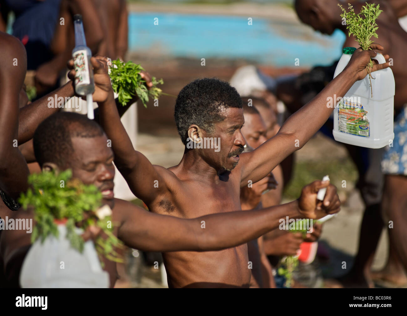 Un groupe d'hommes qui occupent le haut des herbes fraîches et de l'eau pendant un festival vaudou sur la plage en Haïti. Banque D'Images