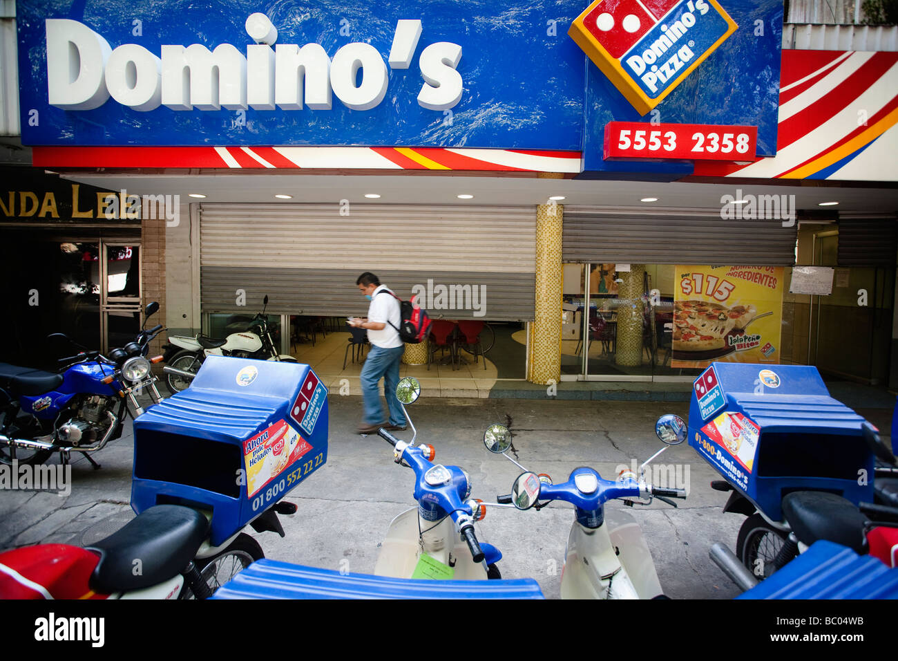 Un homme marche dans la rue entre certains garé les motos et un restaurant Pizza fermé dans la ville de Mexico, DF, Mexique. Banque D'Images