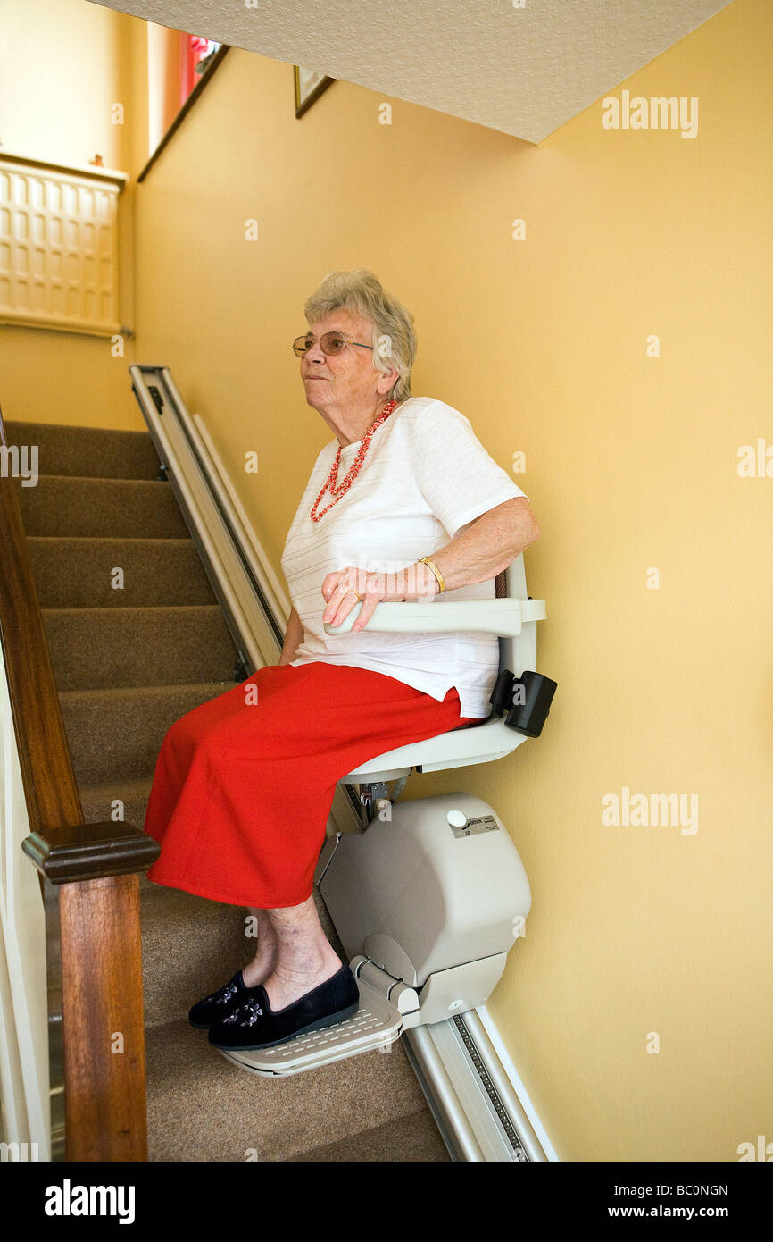 Une vieille dame utilise un télésiège pour monter et descendre les escaliers dans sa maison Banque D'Images
