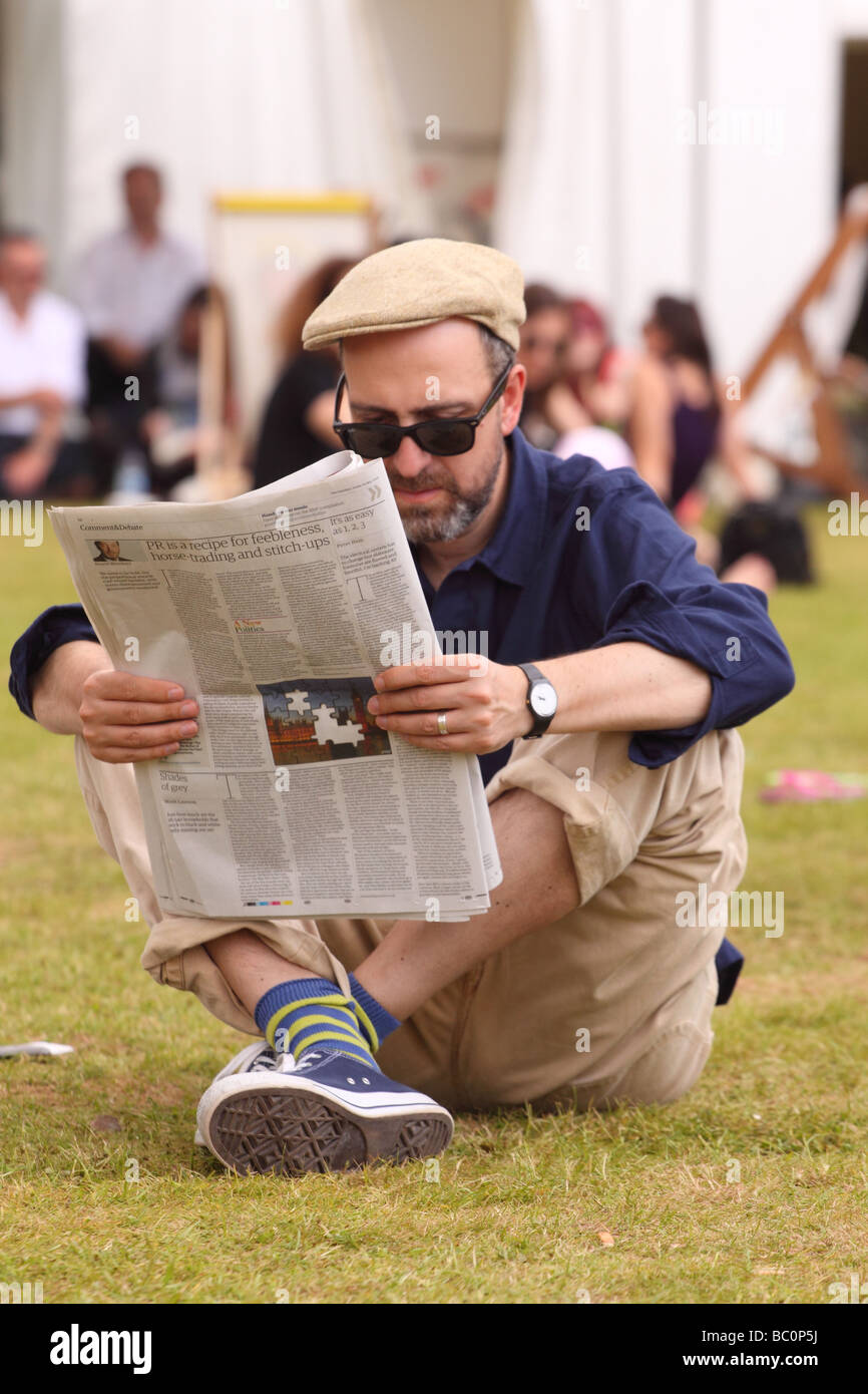 Hay Festival visiteur mâle un journal lecture reposant sur l'herbe pelouse au soleil à Hay-on-Wye fête du livre Banque D'Images