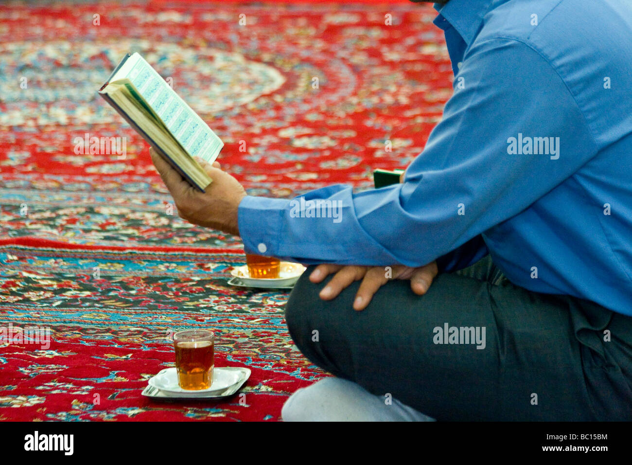 L'homme de boire du thé et de la lecture du Coran dans une petite mosquée de Yazd, Iran Banque D'Images