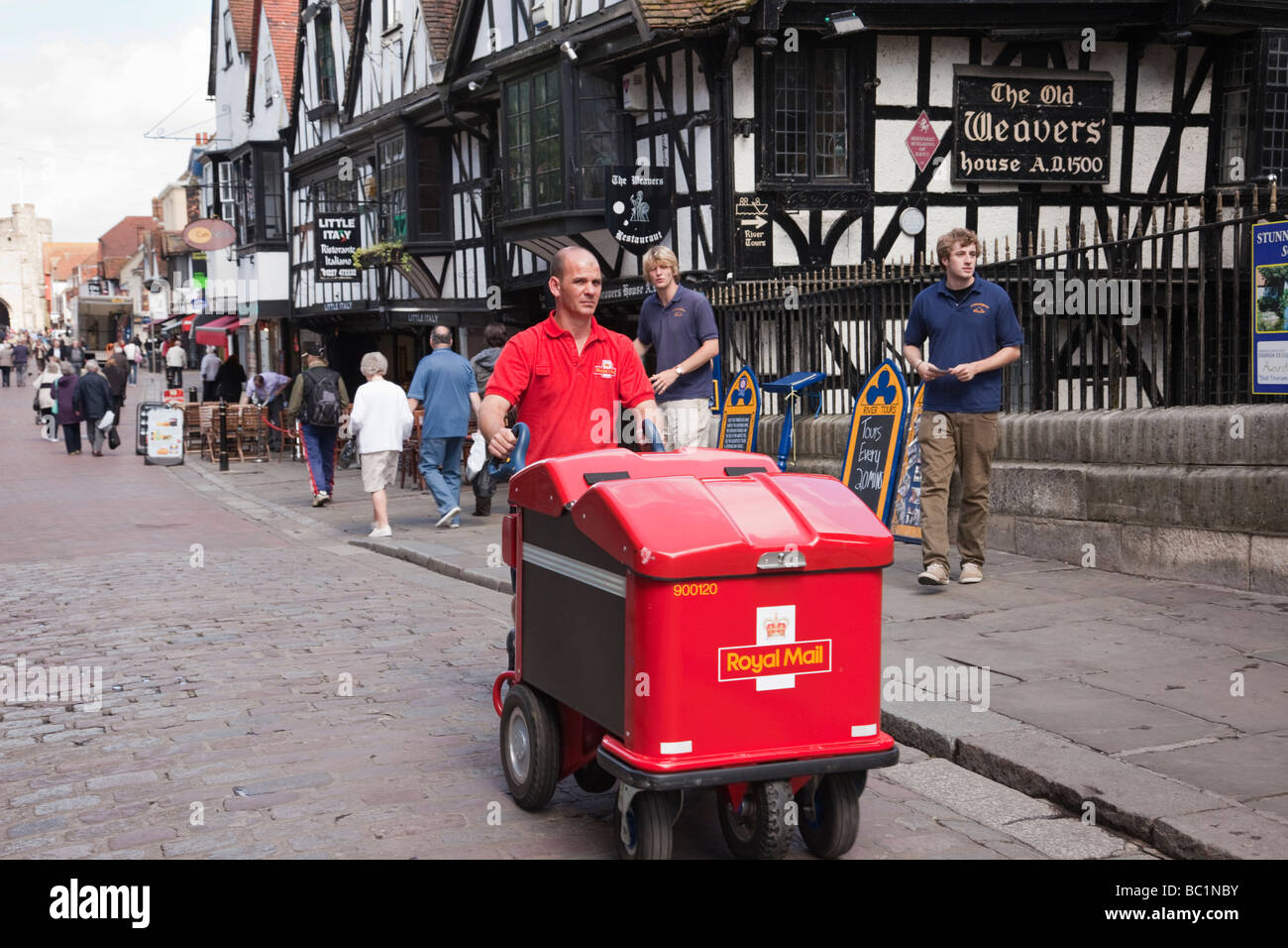 Un facteur poussant un chariot de poste Royal Mail livrer le courrier dans une rue de la ville. Canterbury Kent Angleterre Royaume-uni Grande-Bretagne Banque D'Images