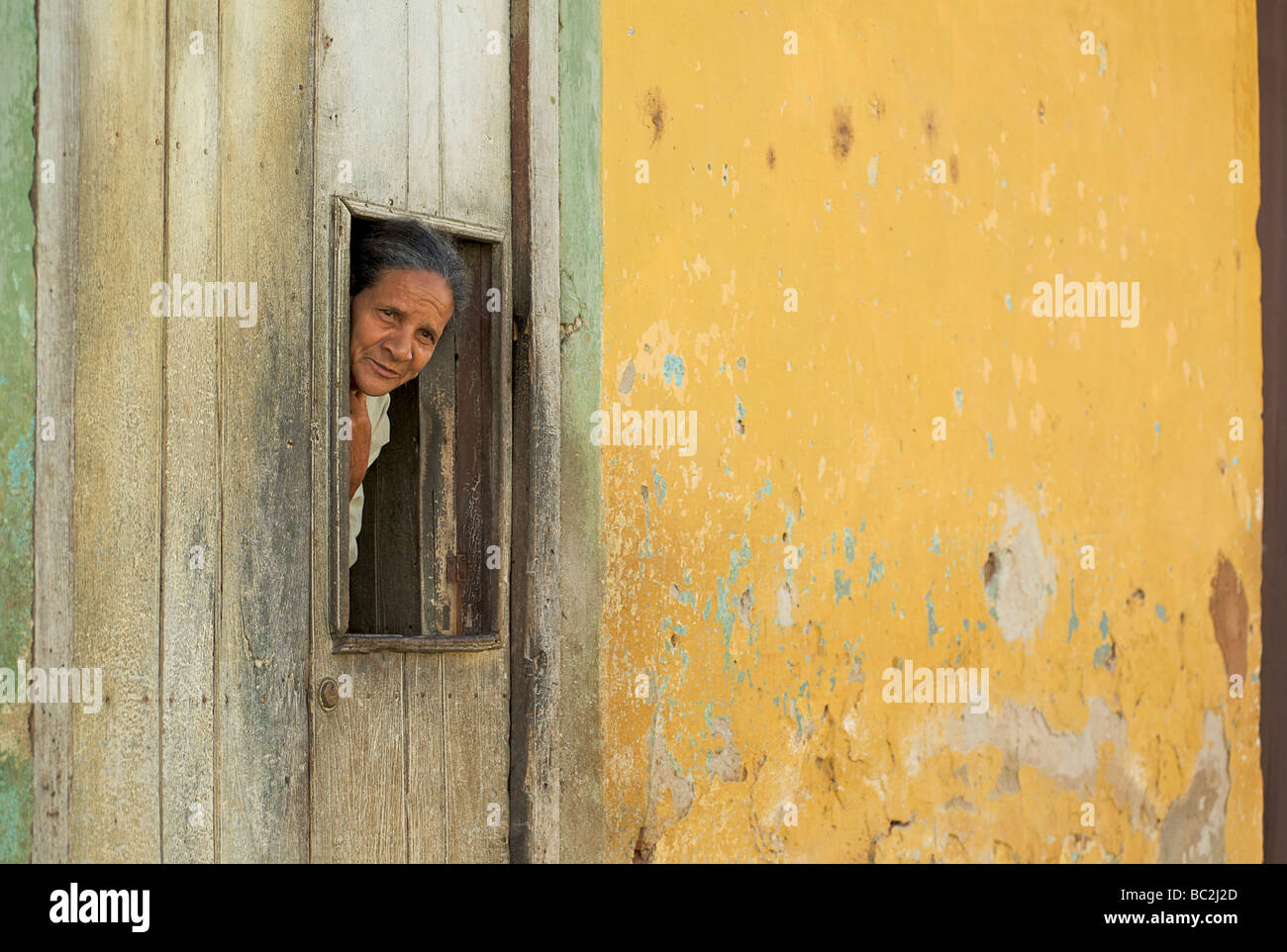 Cuban woman peering d'un panneau situé dans la porte de son peintes de couleurs vives maison coloniale. Trinidad, Cuba Banque D'Images