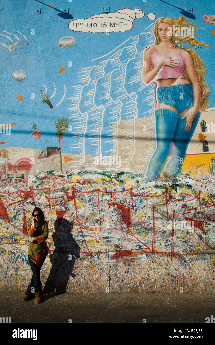 Parler sur un téléphone cellulaire en face d'une peinture murale par R Cronk Venice Beach Los Angeles County California United States of America Banque D'Images
