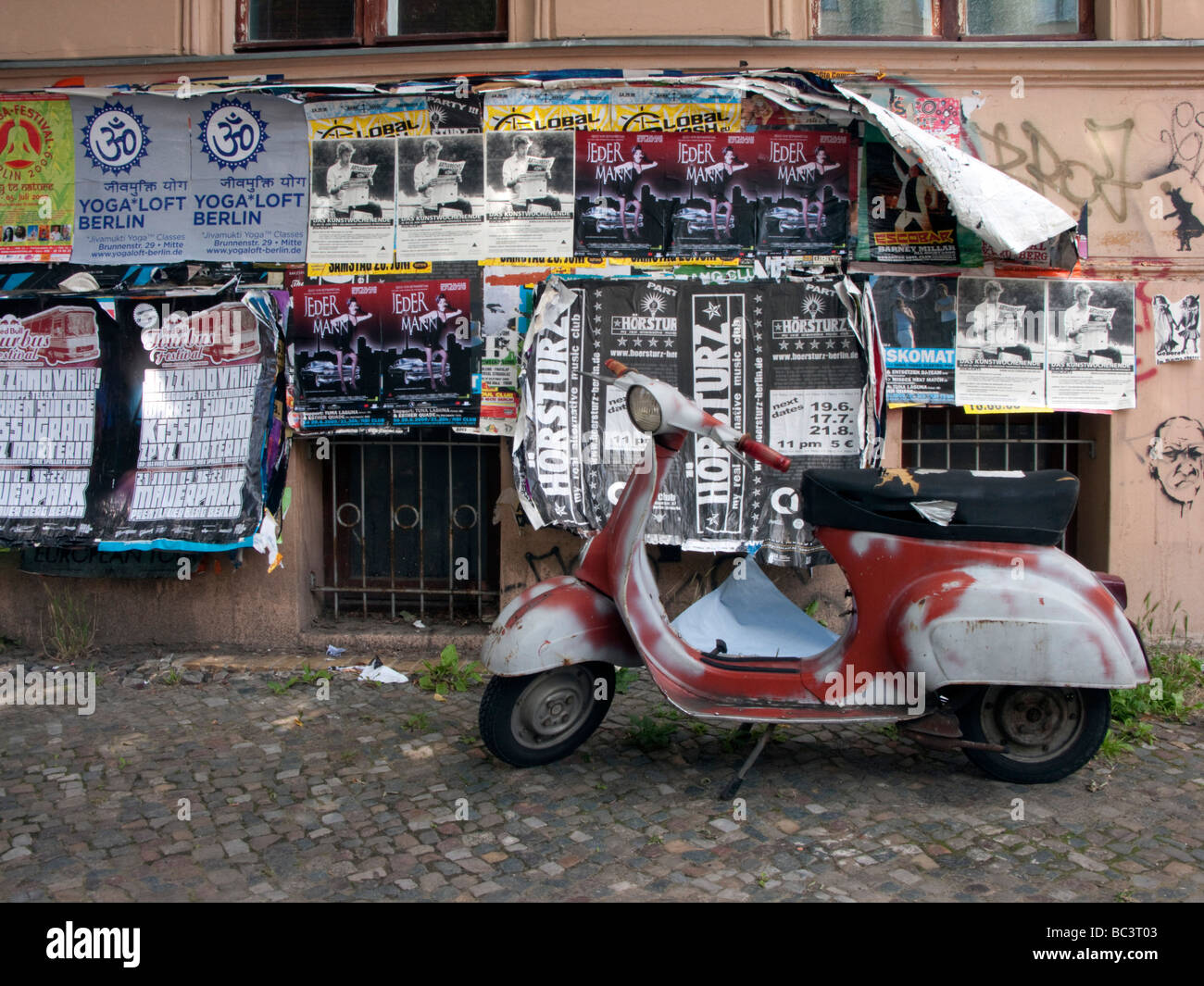 Vieux scooter garé contre mur recouvert de posters dans quartier bohème de Prenzlauer Berg à Berlin Banque D'Images