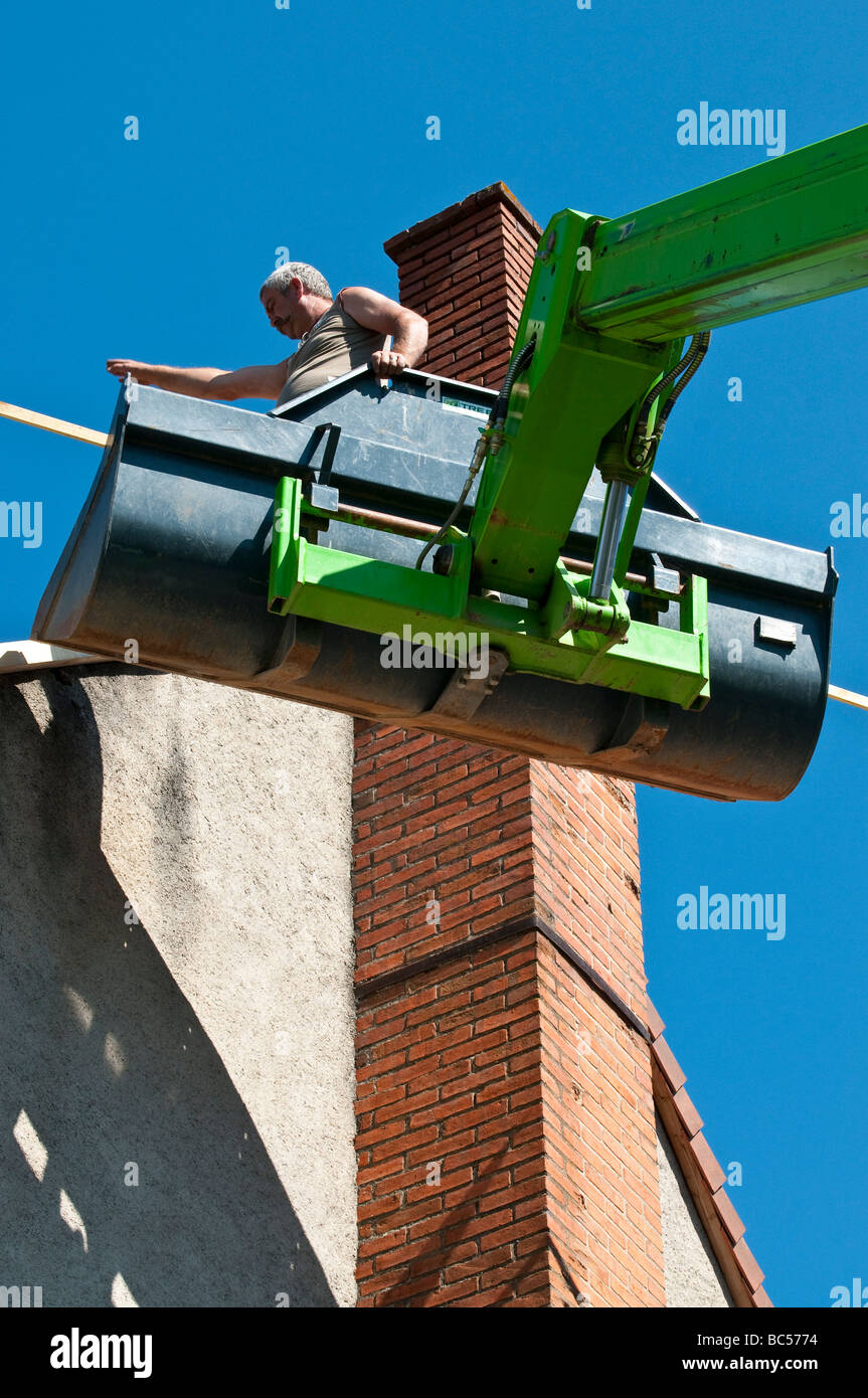 Entrepreneur en construction dans la benne de l'extension de la réparation de grue à flèche toit de maison - France. Banque D'Images