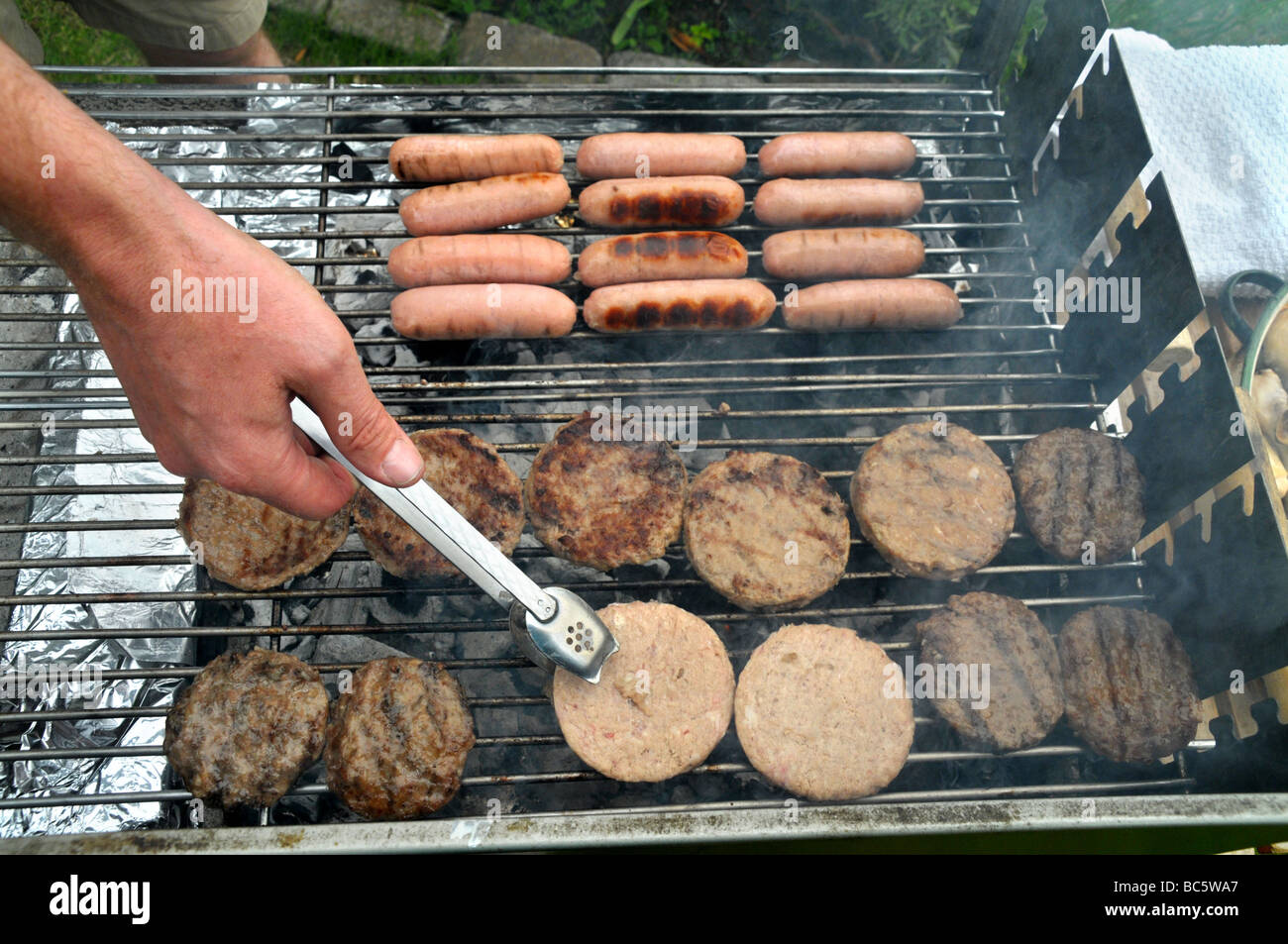 Un homme a tendance à faire un barbecue beefburgers. Banque D'Images