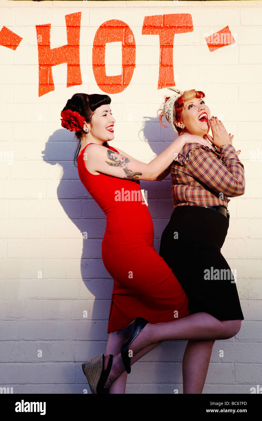 2 jeunes femmes habillées dans un style rétro de rire devant un mur avec le  mot sex sur elle Photo Stock - Alamy