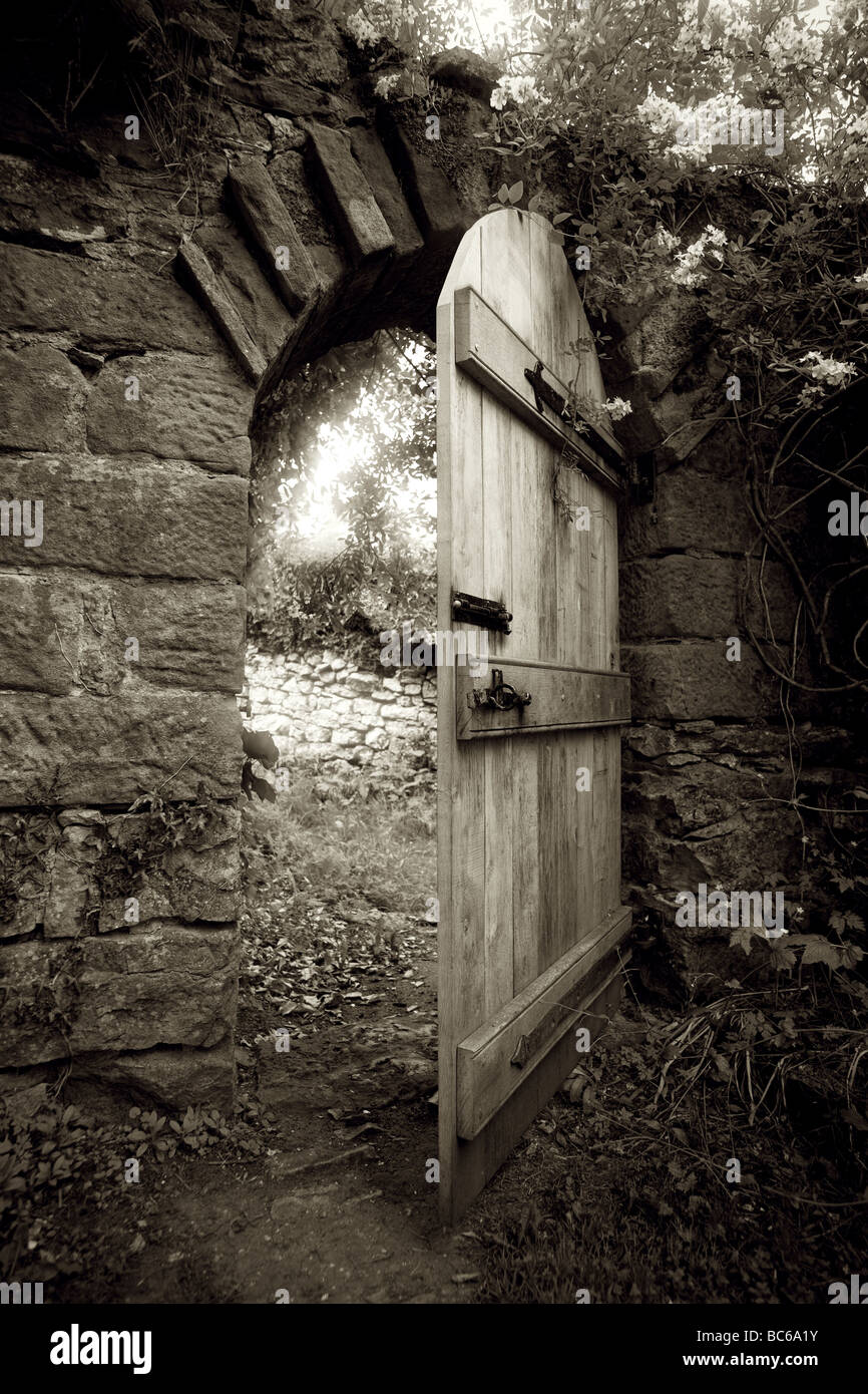 Sepia shot de la moitié traditionnel chêne ouvert porte dans un mur en pierre avec jardin entoure et arch, surplombés de plantes et de lierre Banque D'Images