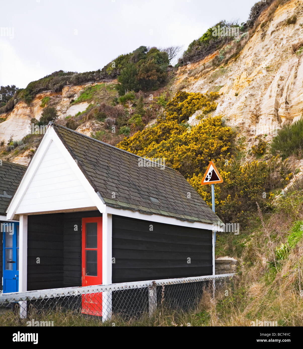 Cabines de plage à la base de l'érosion des falaises. Un signe derrière les huttes met en garde contre le danger de chutes de pierres. Front de mer de Bournemouth. Banque D'Images