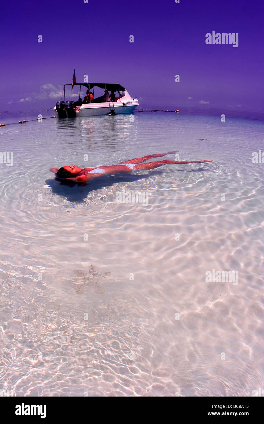 Fille en bikini blanc flottant dans l'eau peu profonde avec fond de sable. Boatin plongée et aux pépites de chocolat Starfish, Protoreaster nodosus Banque D'Images