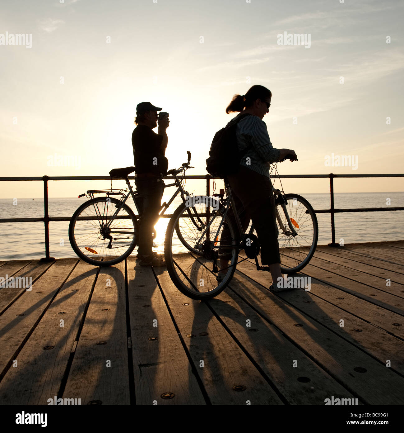Silhouette de deux personnes à vélo contre le soleil couchant aberystwyth Wales UK Banque D'Images