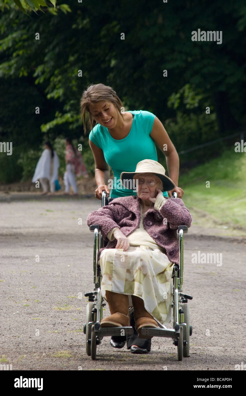 Jeune femme poussant dame âgée en fauteuil roulant dans park Banque D'Images