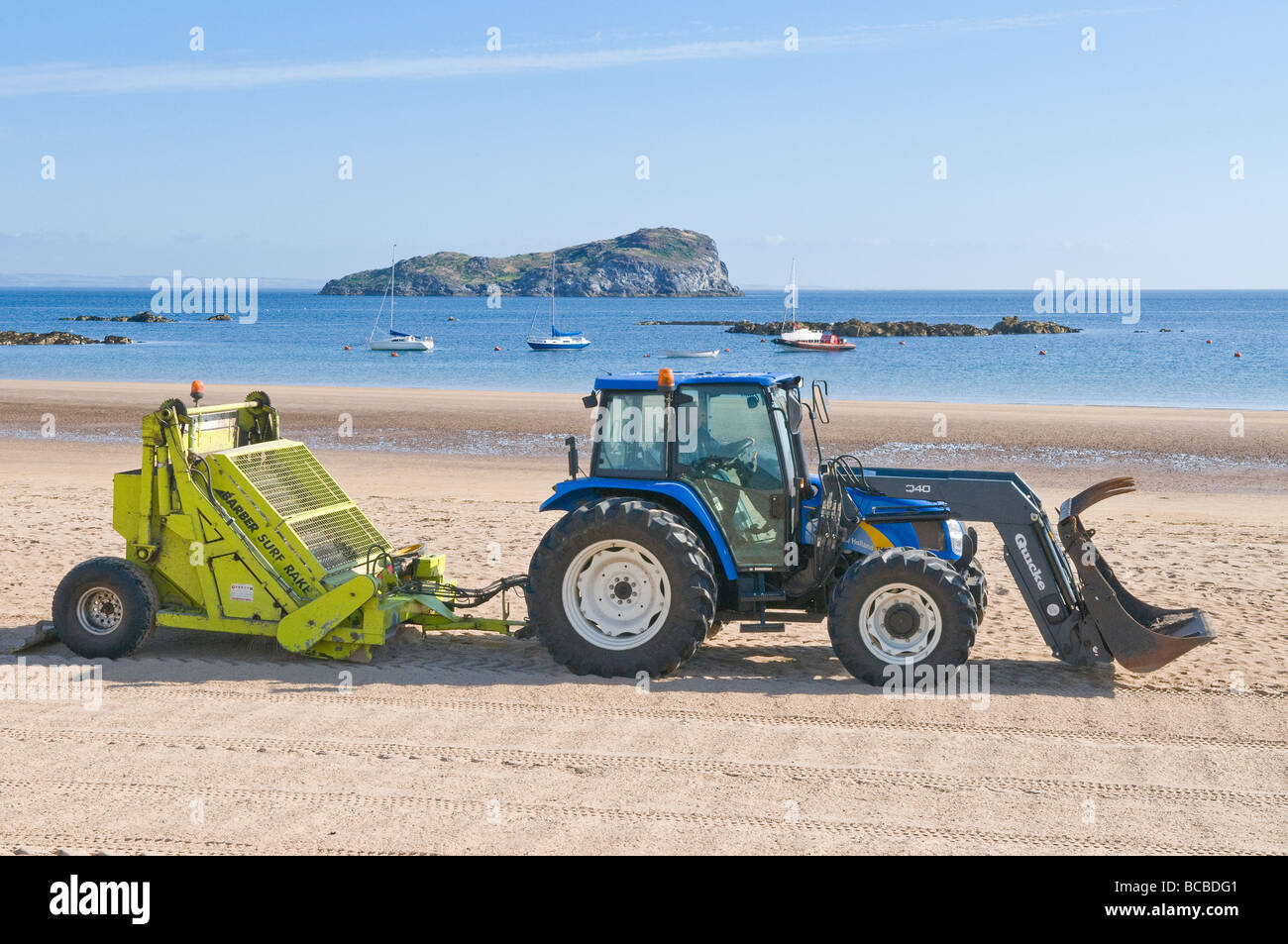Le tracteur tirant un râteau mécanique pour enlever les ordures et les algues d'une plage à North Berwick en Écosse. Banque D'Images