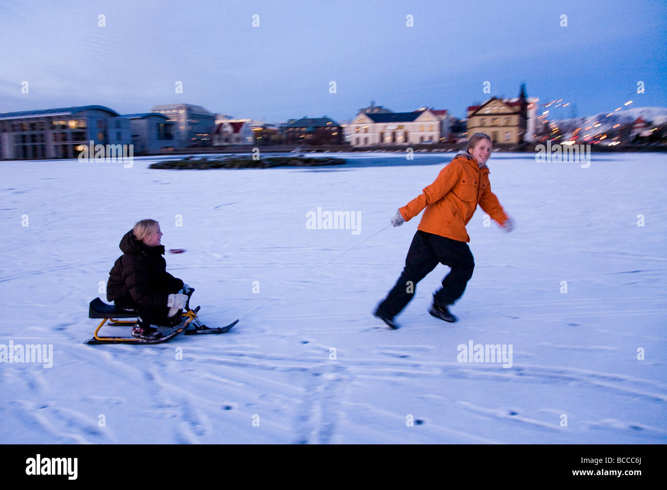 Deux jeunes filles, jouant sur un traîneau neige sur un lac gelé du centre-ville de Tjornin Reykjavik Islande Banque D'Images