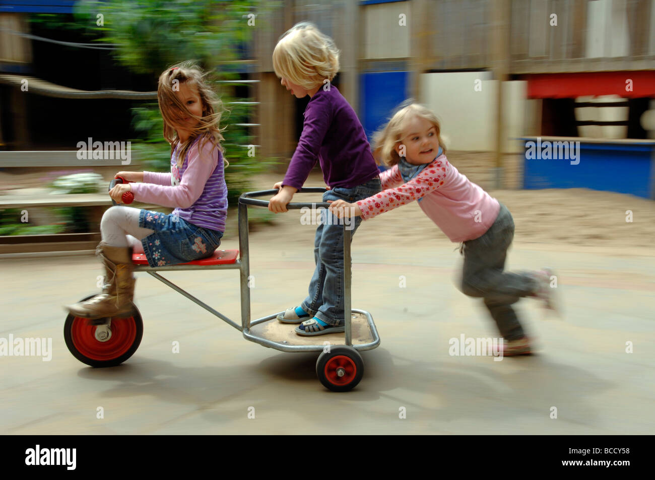 Les enfants et l'enseignant joue sur une aire de jeux dans un jardin d'un jour d'été. Banque D'Images