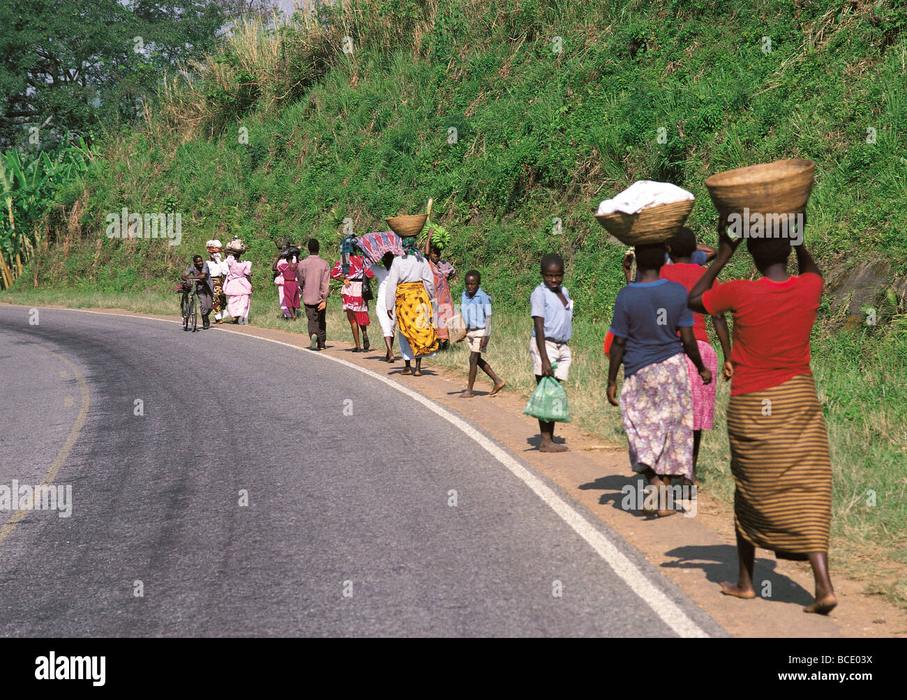 La population locale et des femmes portant des charges de la tête aux pieds nus le long de la route côté à marché près de Kabale en Ouganda du sud-ouest de l'Afrique de l'Est Banque D'Images