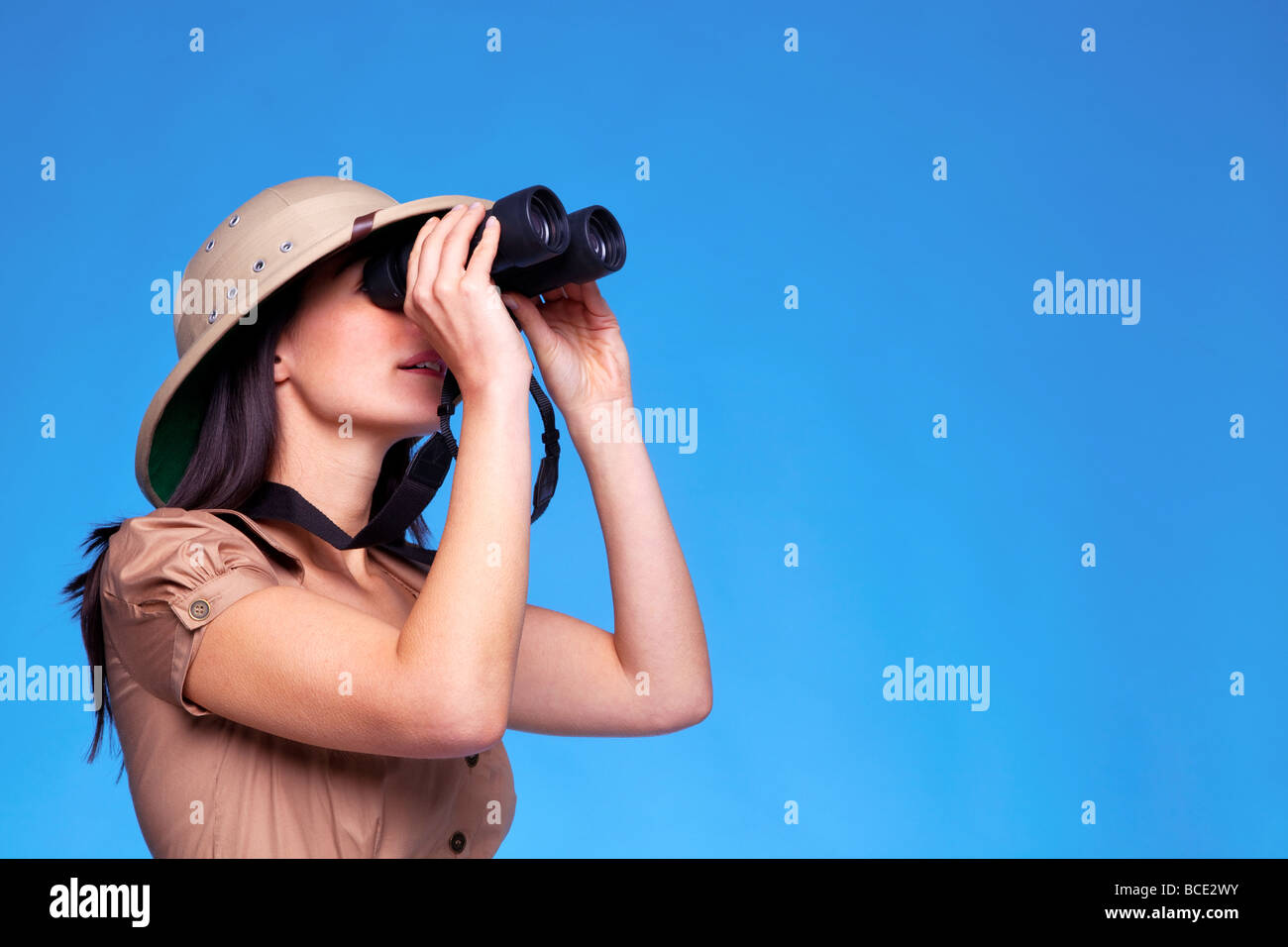 Une femme portant un casque colonial à travers une paire de jumelles à fond bleu avec copie espace Banque D'Images