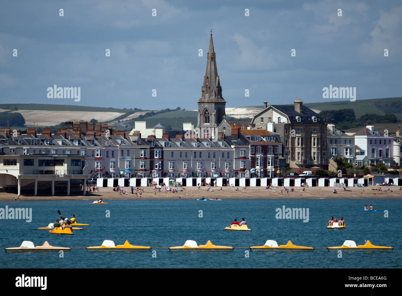 Avis de pédalos en face de la plage de sable et la flèche de l'église St.Jonh à Weymouth Dorset Banque D'Images