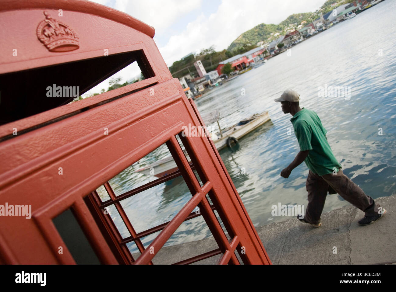 Un homme local passe devant un téléphone colonial abandonné à St George, Grenade (Caraïbes) avec une vue imprenable sur le port et les bateaux de pêche. Banque D'Images