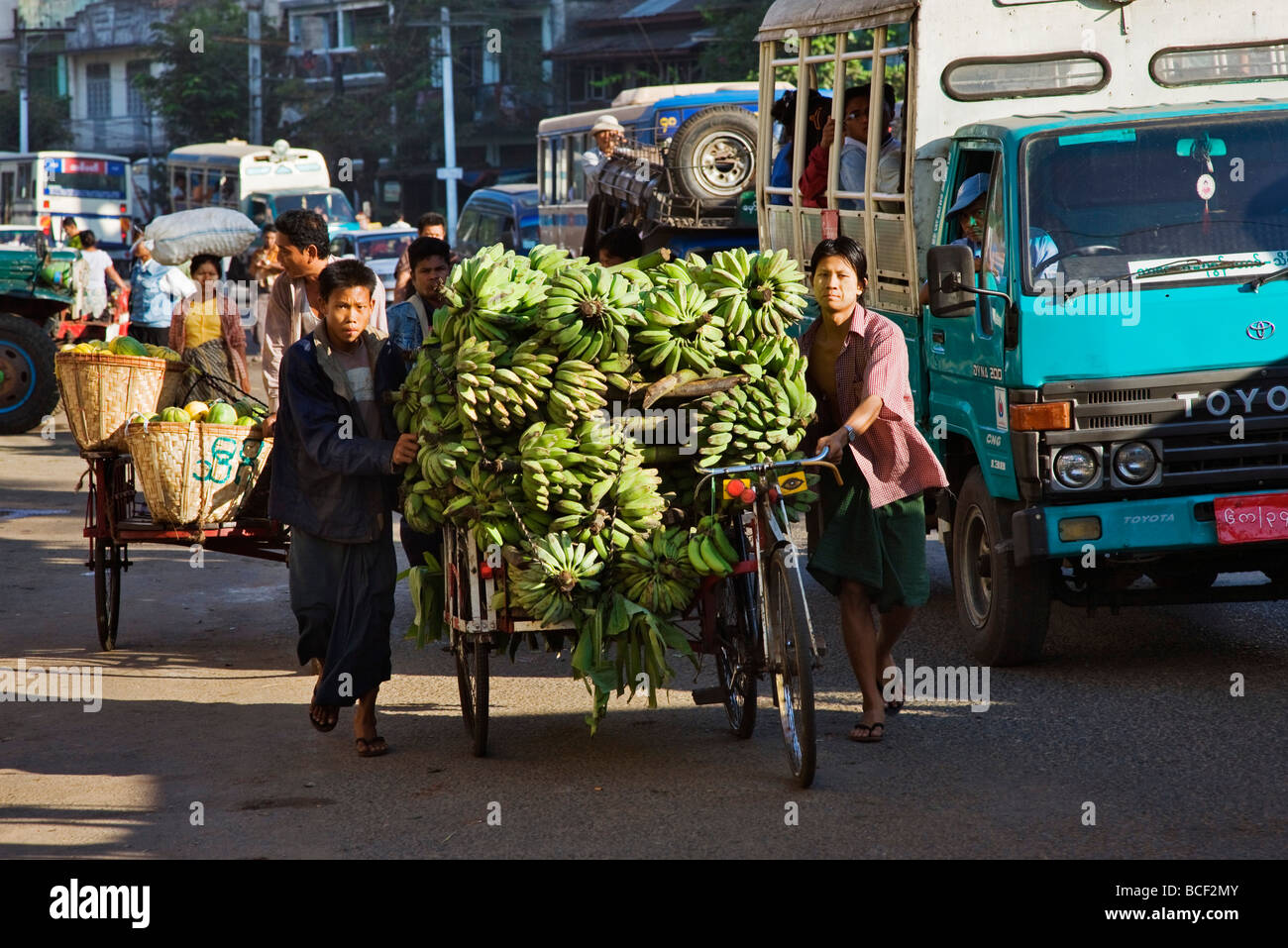 Le Myanmar, Birmanie, Yangon. Une longue scène de rue à Yangon avec trishaws laden avec fruit la position de marché. Banque D'Images