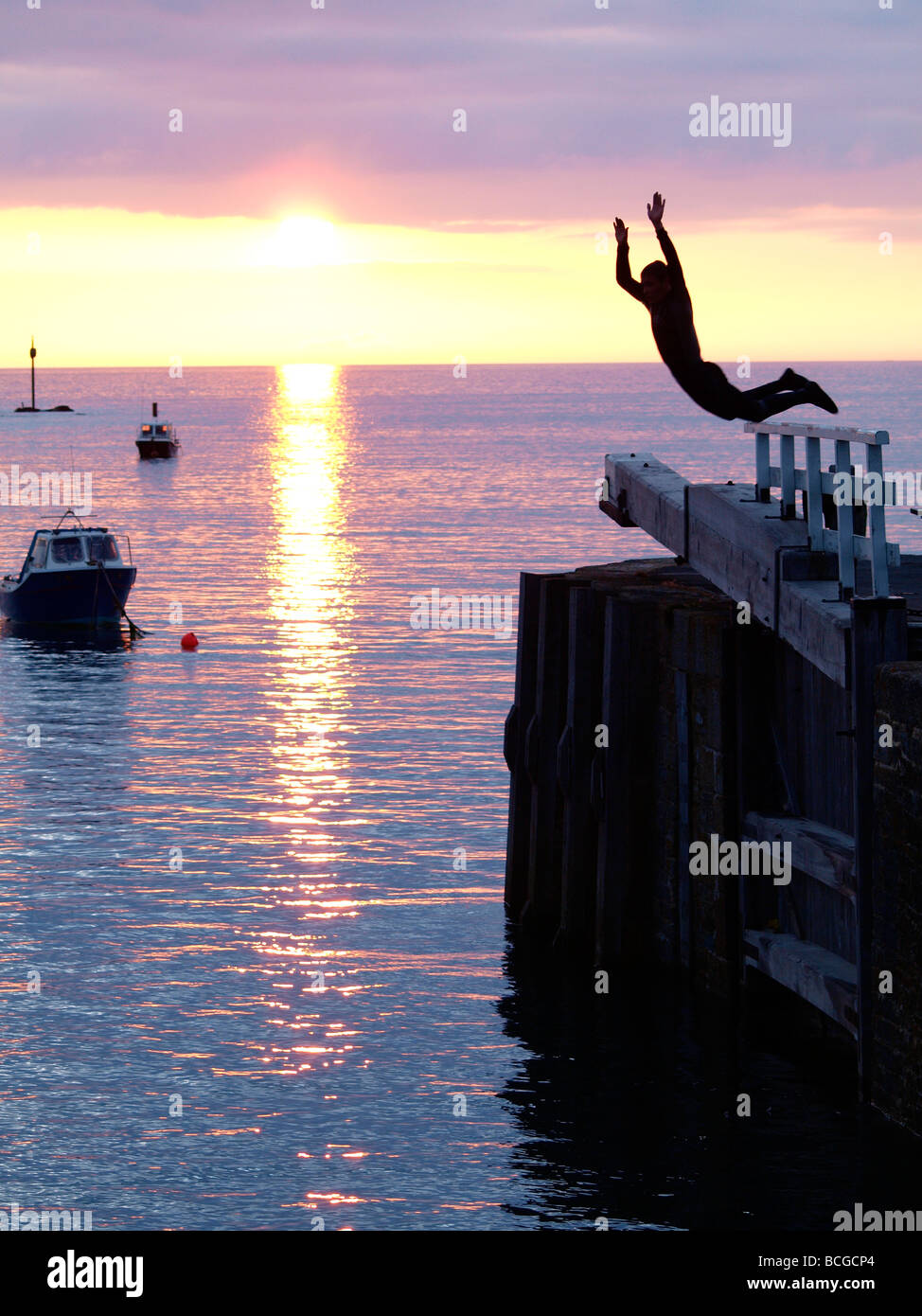 Adolescent sautant d'écluses dans la mer au coucher du soleil Banque D'Images