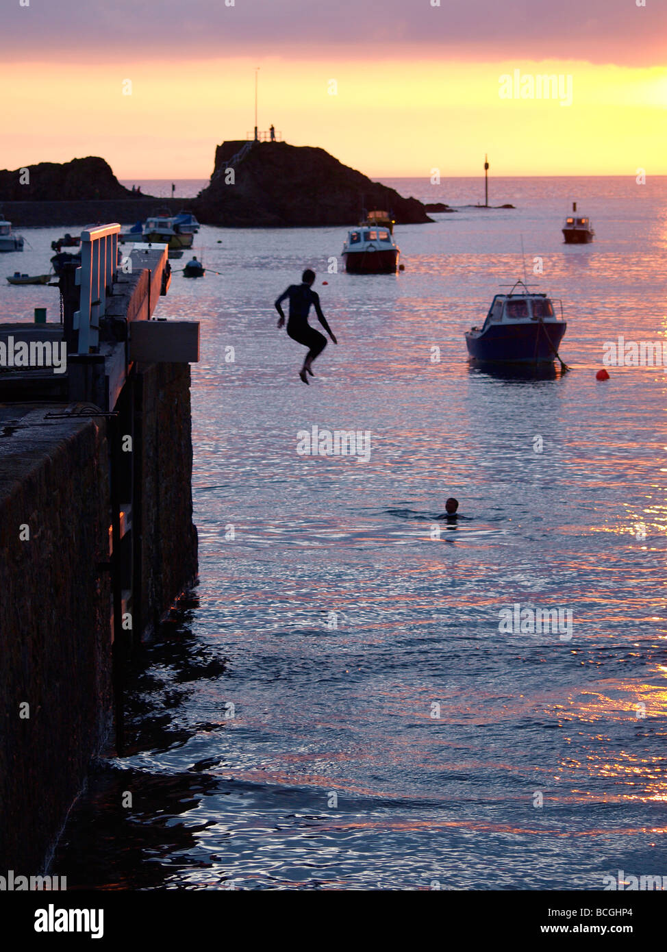 Les adolescents sautant de portes de l'écluse dans la mer au coucher du soleil Banque D'Images