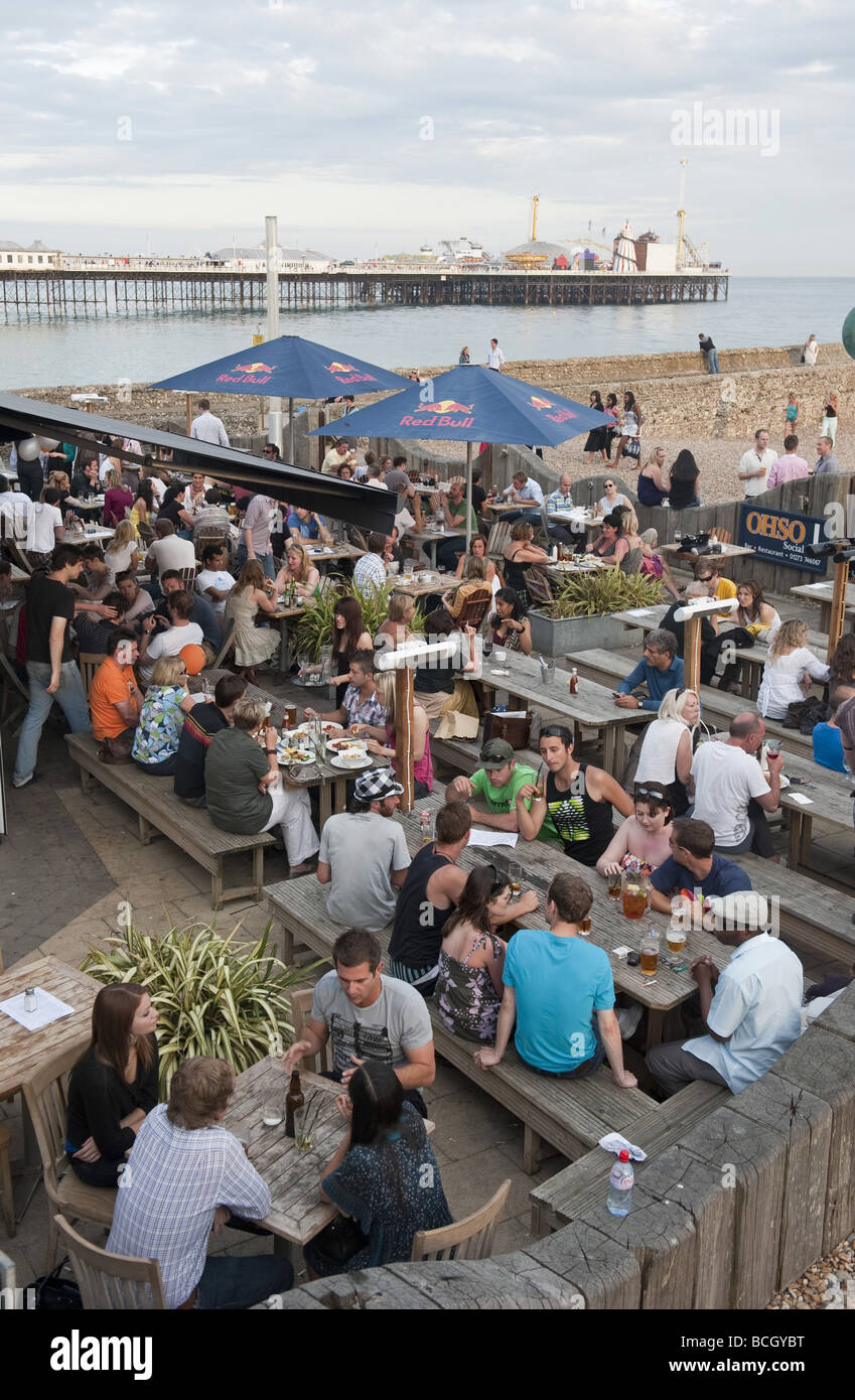 Les jeunes vacanciers et habitants profitez d'une journée ensoleillée à un pub-restaurant sur la plage près de la jetée d'amusement à la ville balnéaire de Brighton Banque D'Images