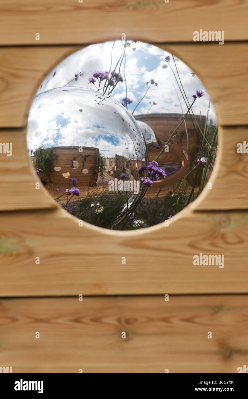 Regarder à travers un trou dans les sphères des panneaux de clôture à Chrome conçu dans un jardin. L'Angleterre Banque D'Images