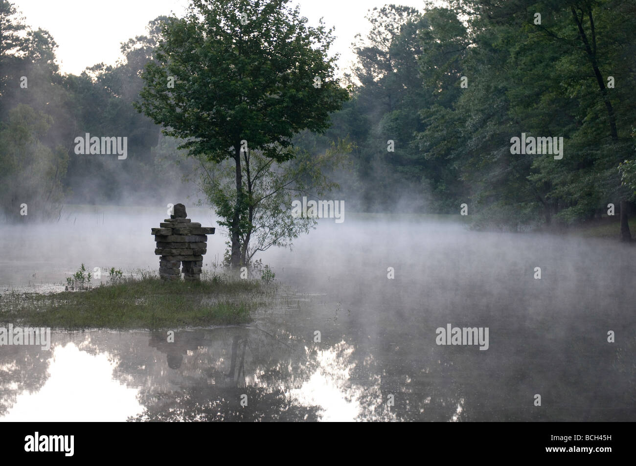 Inukshuk sur une île dans un lac en forêt brumeuse Banque D'Images