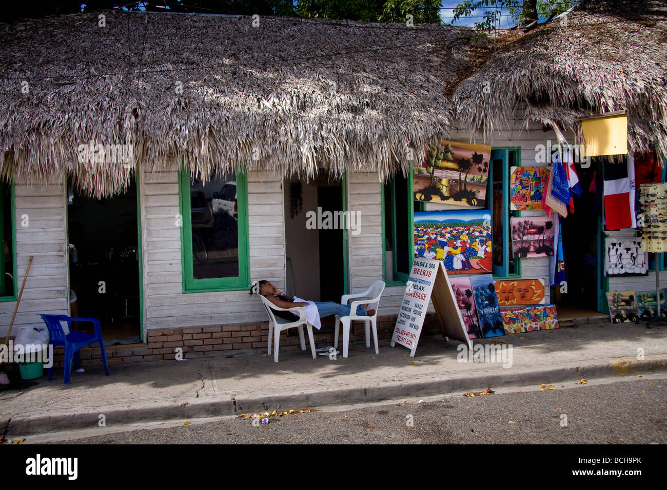 Un vendeur proposant des massages, relaxation et un spa repose sur deux chaises en plastique blanc à l'extérieur de sa boutique à Sosua, Domini Banque D'Images