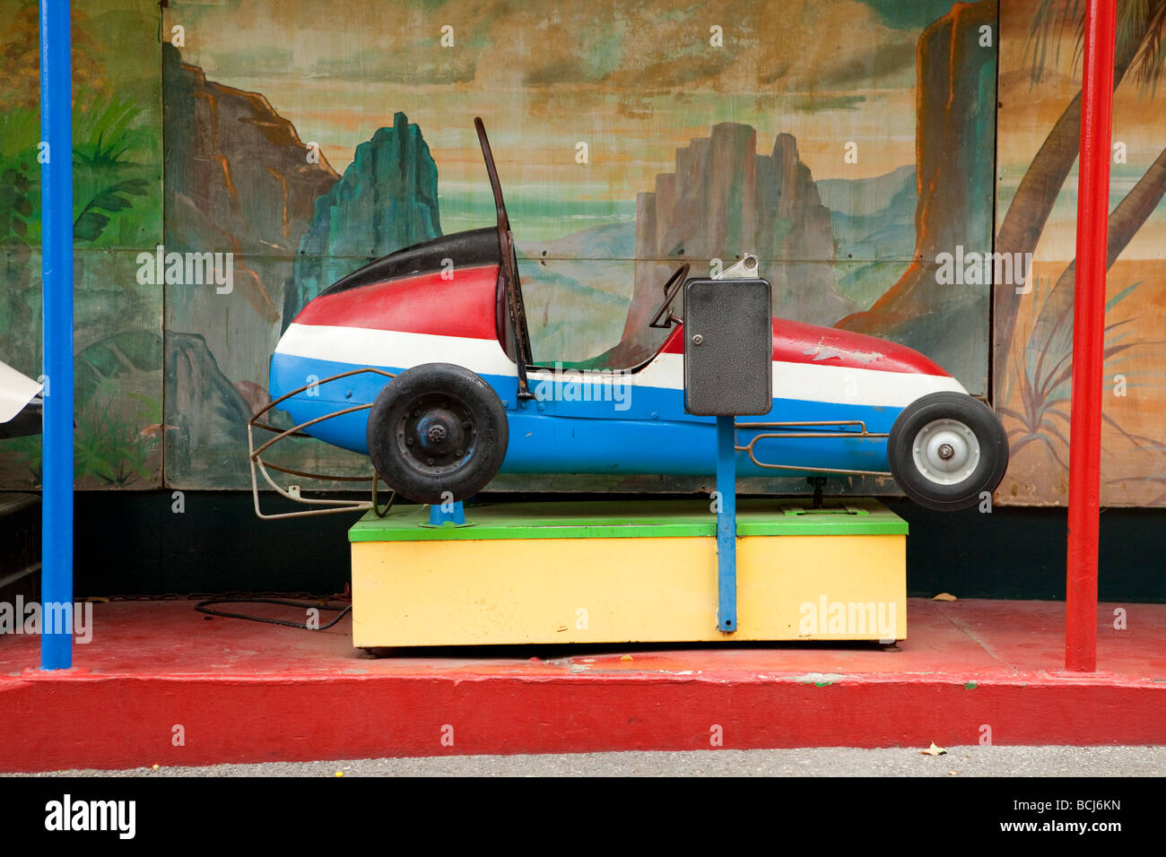 Enfants à monnayeur's ride en forme de voiture de course avec rouge blanc bleu thème couleur reposant sur la plate-forme rouge avec peinture murale Banque D'Images