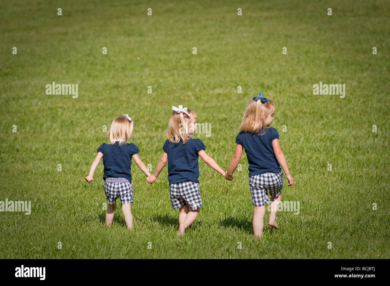 Trois petites filles, sœurs, tenant les mains de marcher ensemble dans les champs tout habillé. Deux des filles sont des jumeaux Banque D'Images