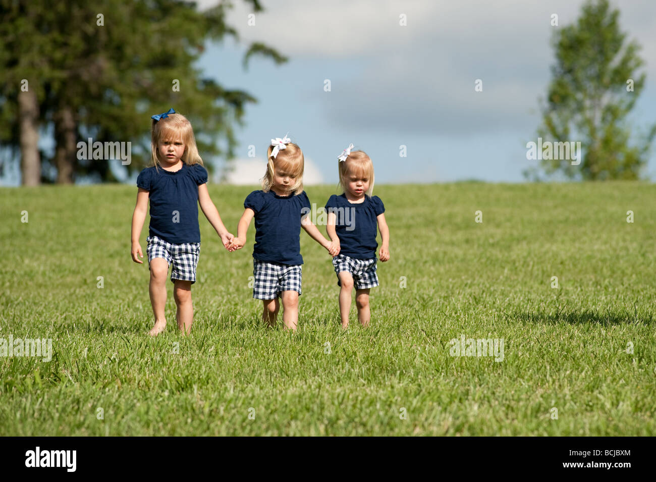 Trois petites filles, sœurs, tenant les mains de marcher ensemble dans les champs tout habillé. Deux des filles sont des jumeaux Banque D'Images