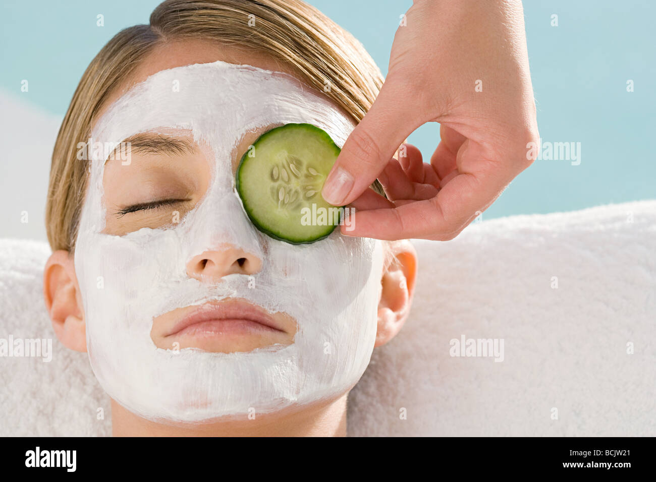 Jeune femme portant un masque du visage avoir tranche de concombre sur eye Banque D'Images