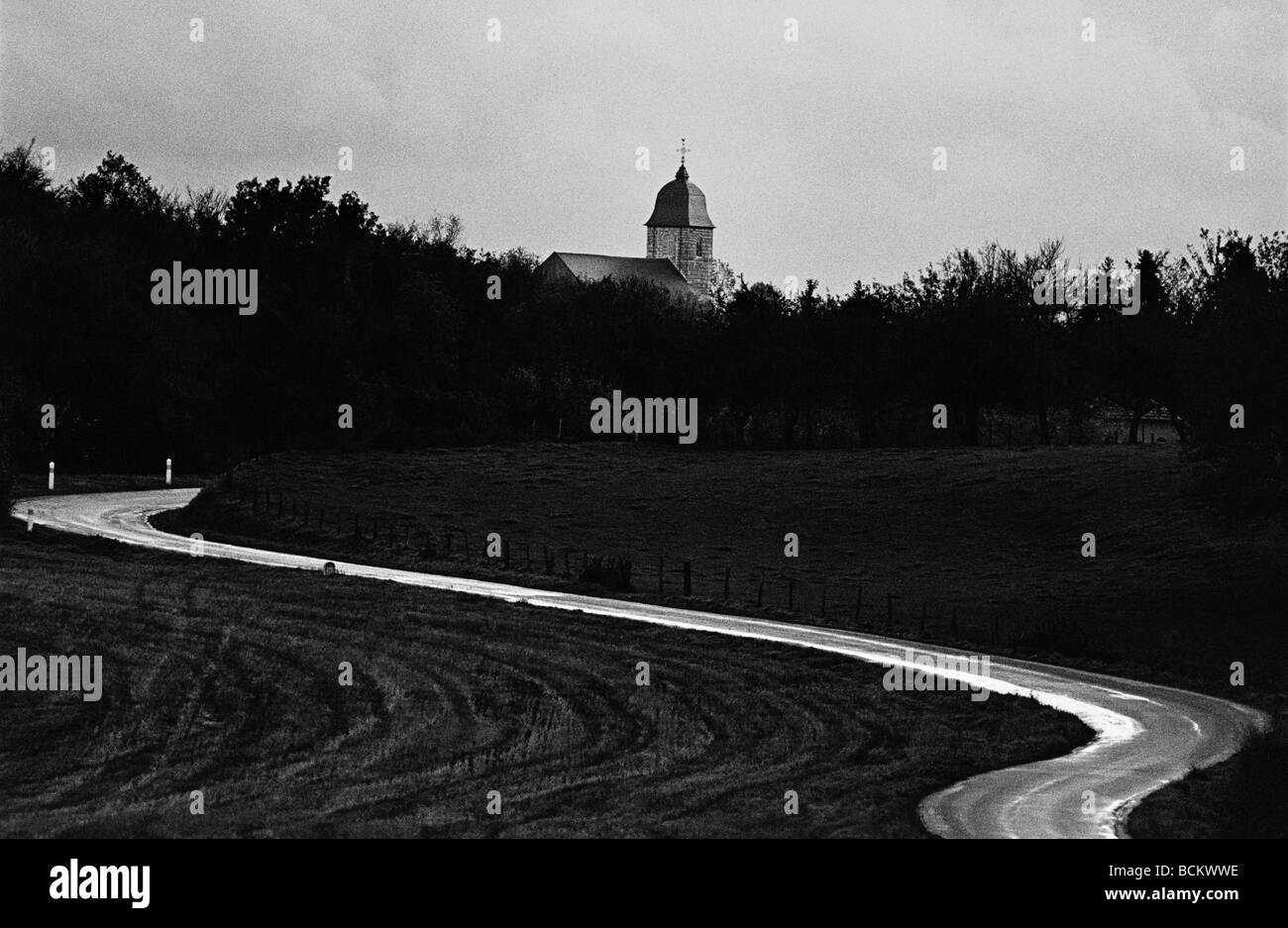 Route sinueuse à travers les arbres, église en arrière-plan, b&w Banque D'Images