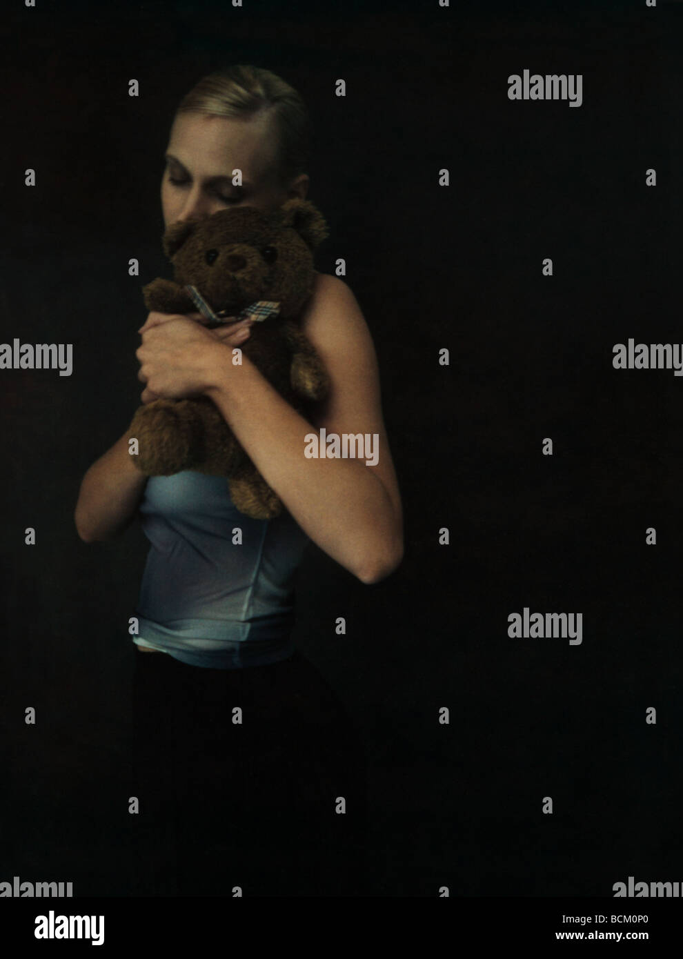 Femme debout dans l'obscurité et hugging teddy bear, les yeux fermés Banque D'Images