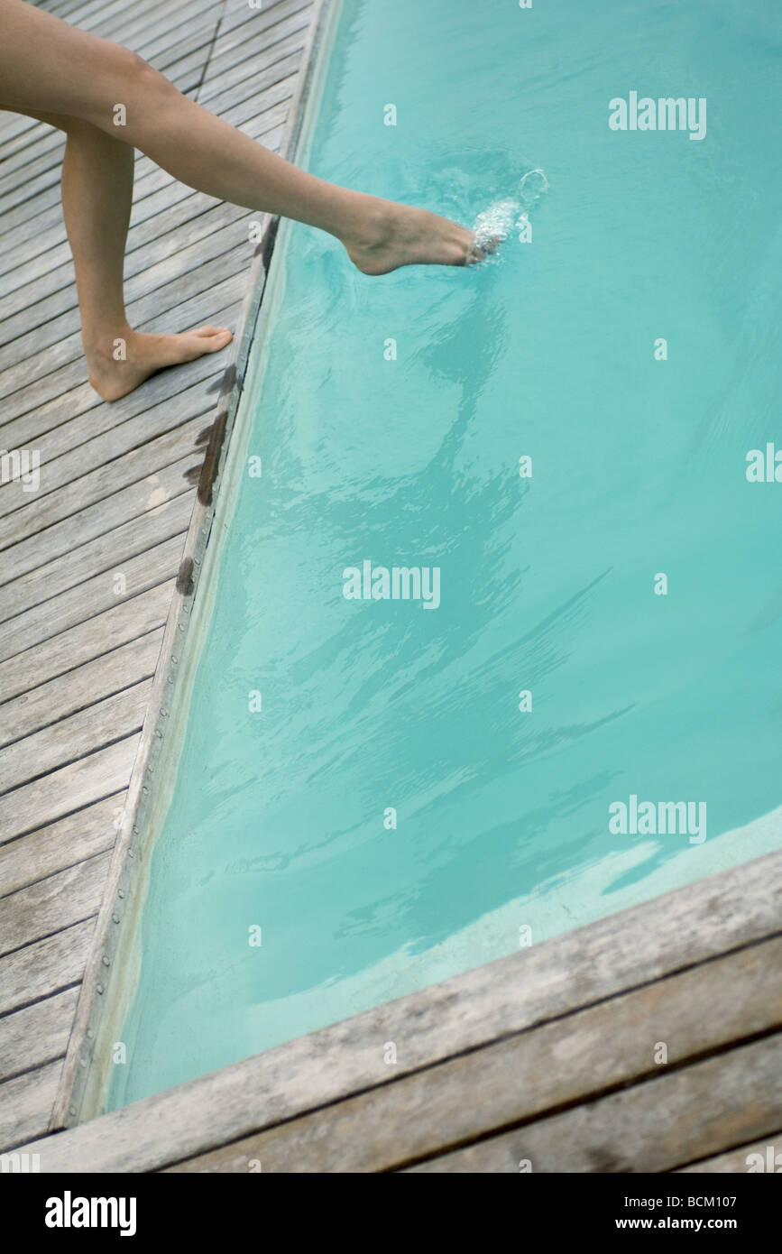 Femme debout à côté de la piscine, plongeant les pieds dans l'eau, low section Banque D'Images
