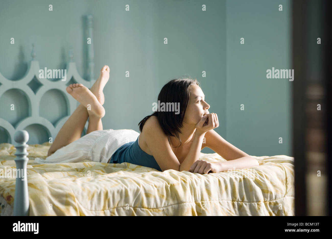 Woman lying on bed with main sous le menton, les jambes Banque D'Images