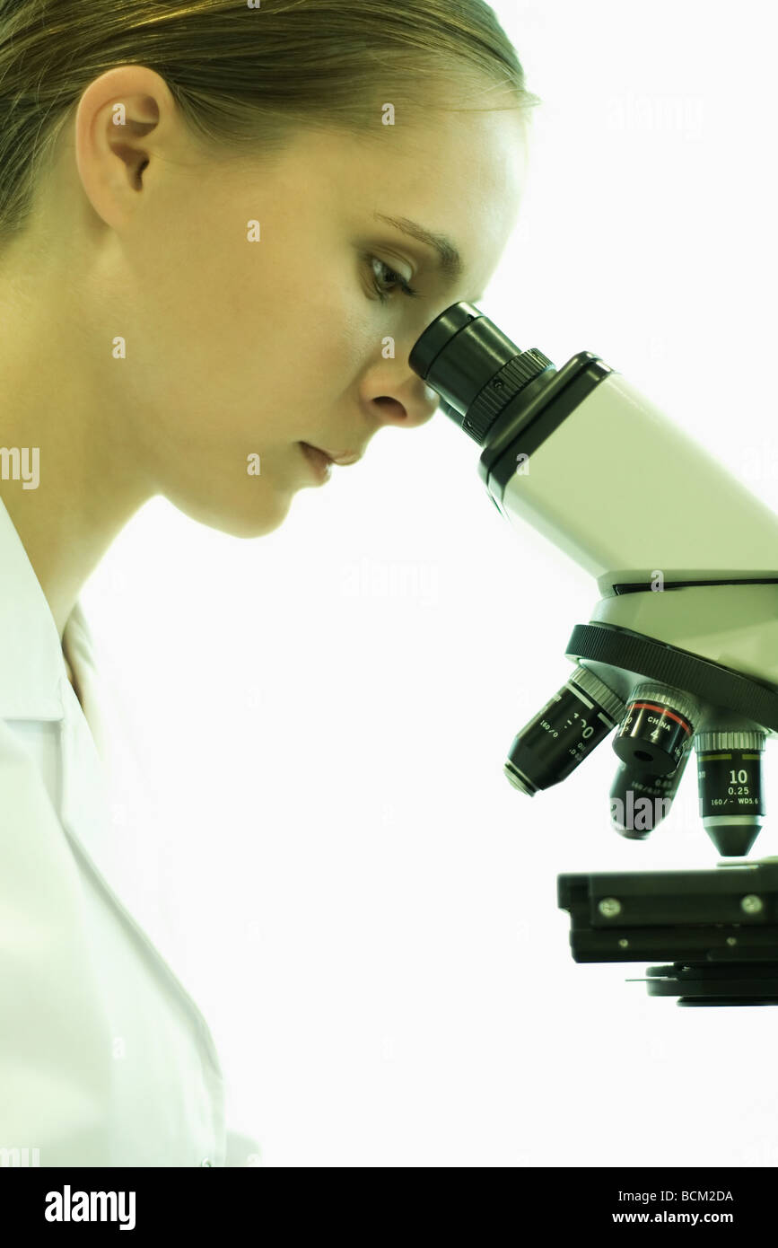 Female scientist looking through microscope, side view Banque D'Images