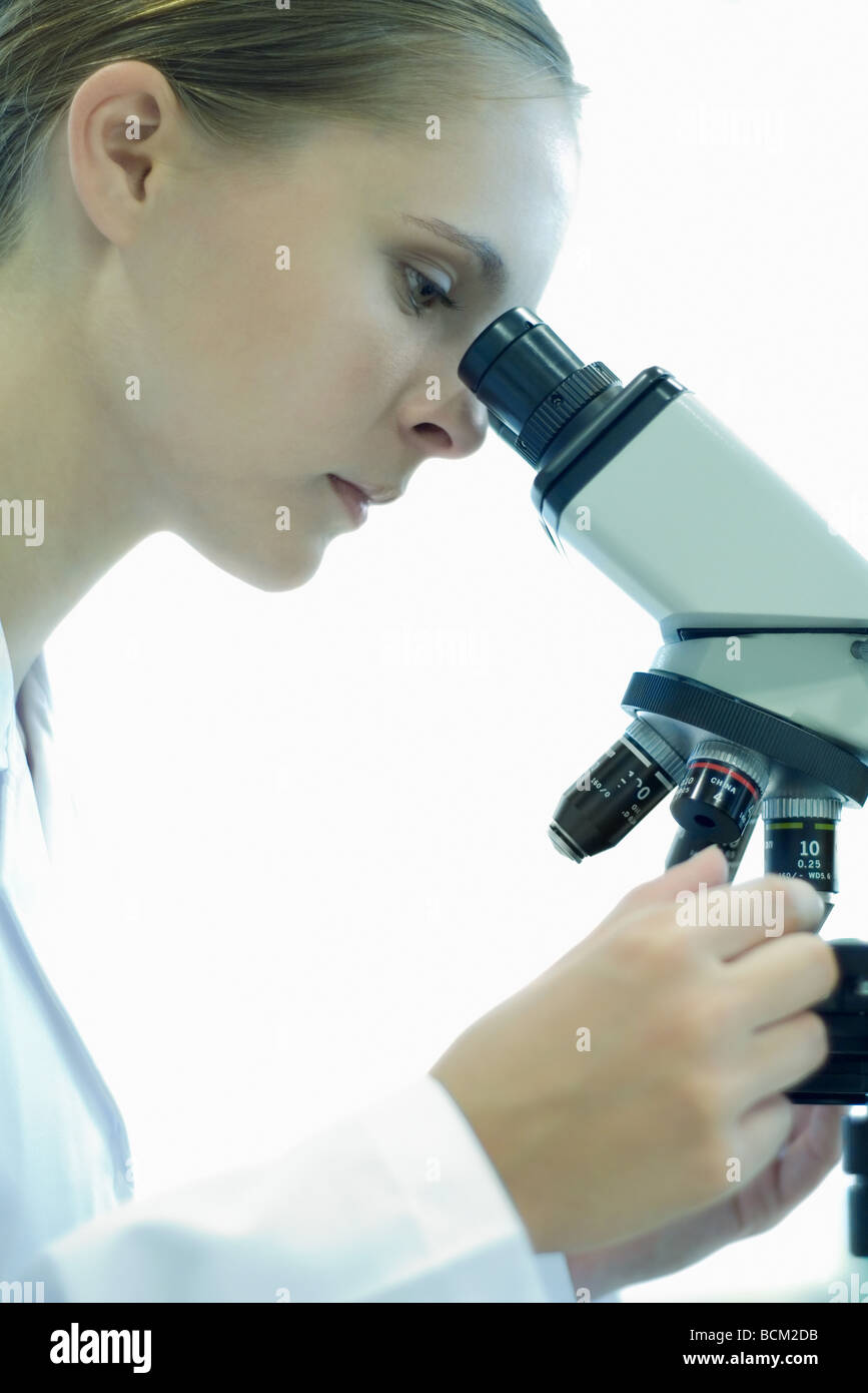 Female scientist looking through microscope, side view Banque D'Images